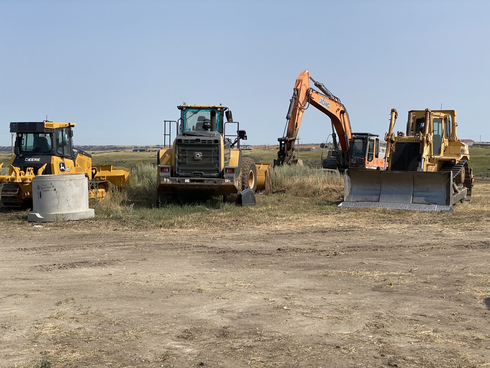 Two dozers, a wheel loader and an excavator parked at the edge of the yard, with open prairie behind