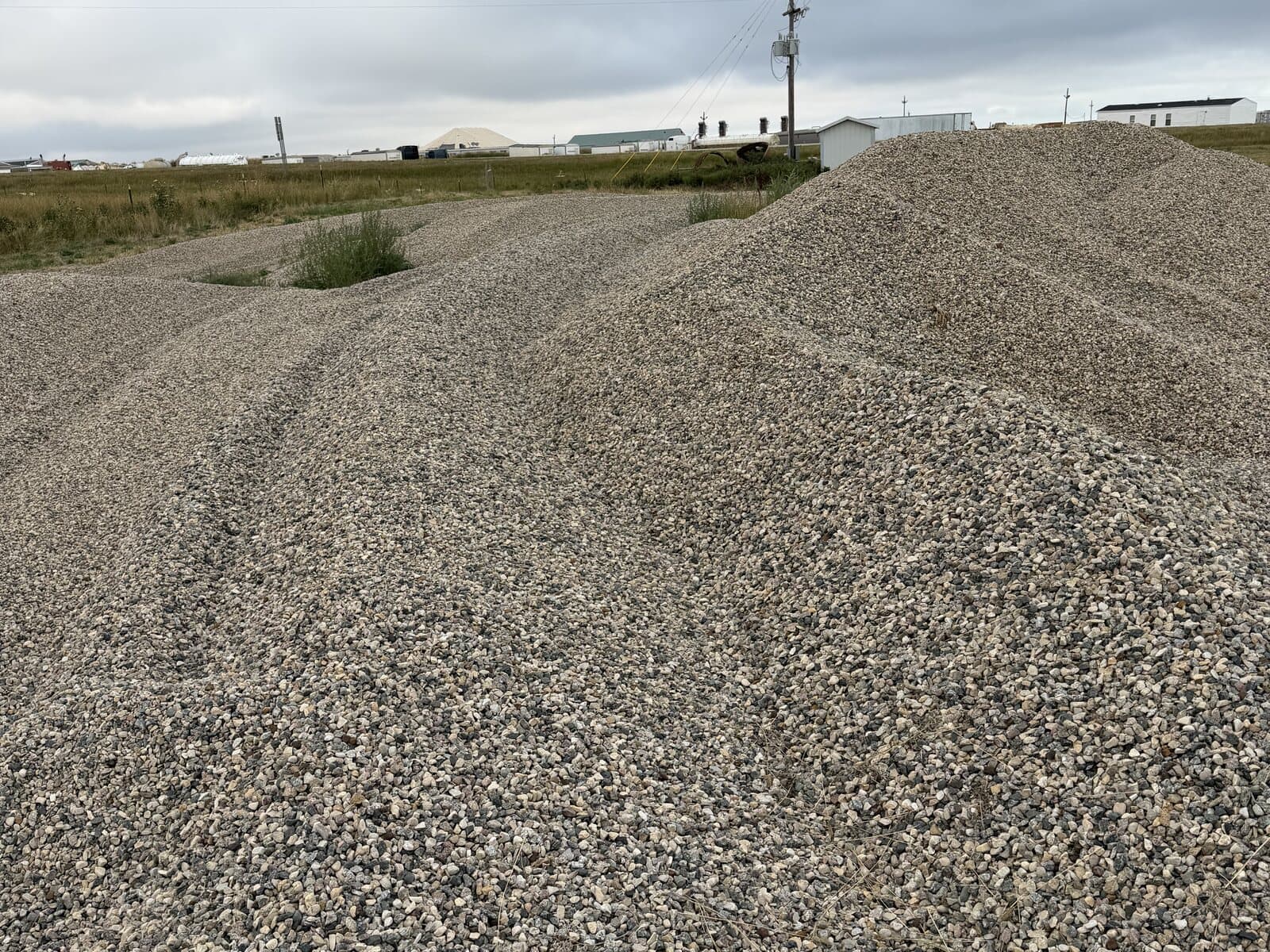 A gravel stockpile with buildings and a power line behind it
